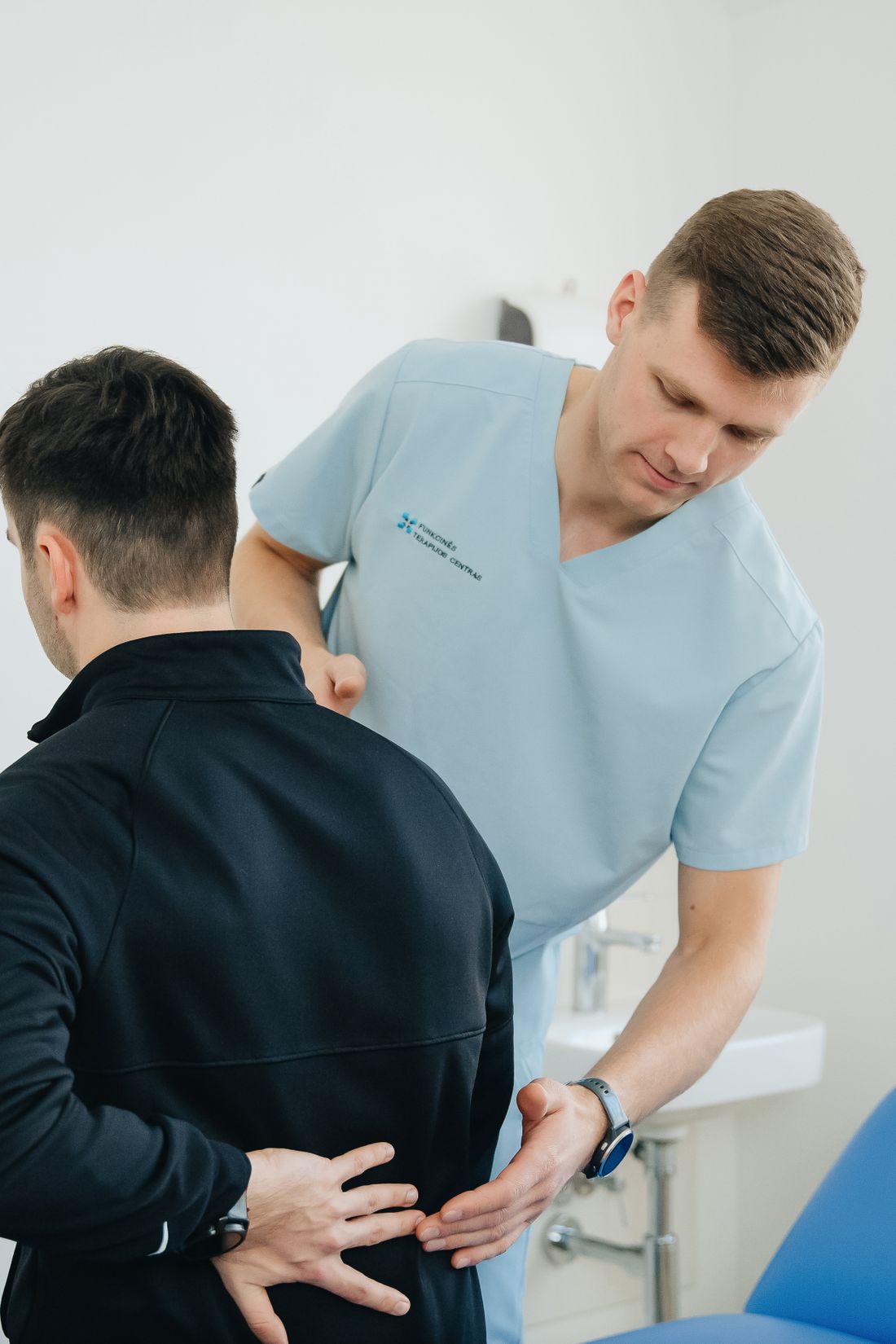 Owen checking a patient's lower back movement while standing behind him