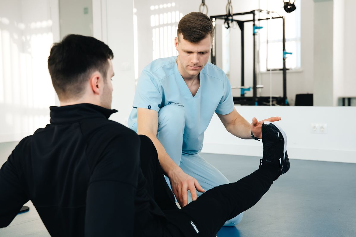 Owen guiding a patient through a leg exercise on the gym floor